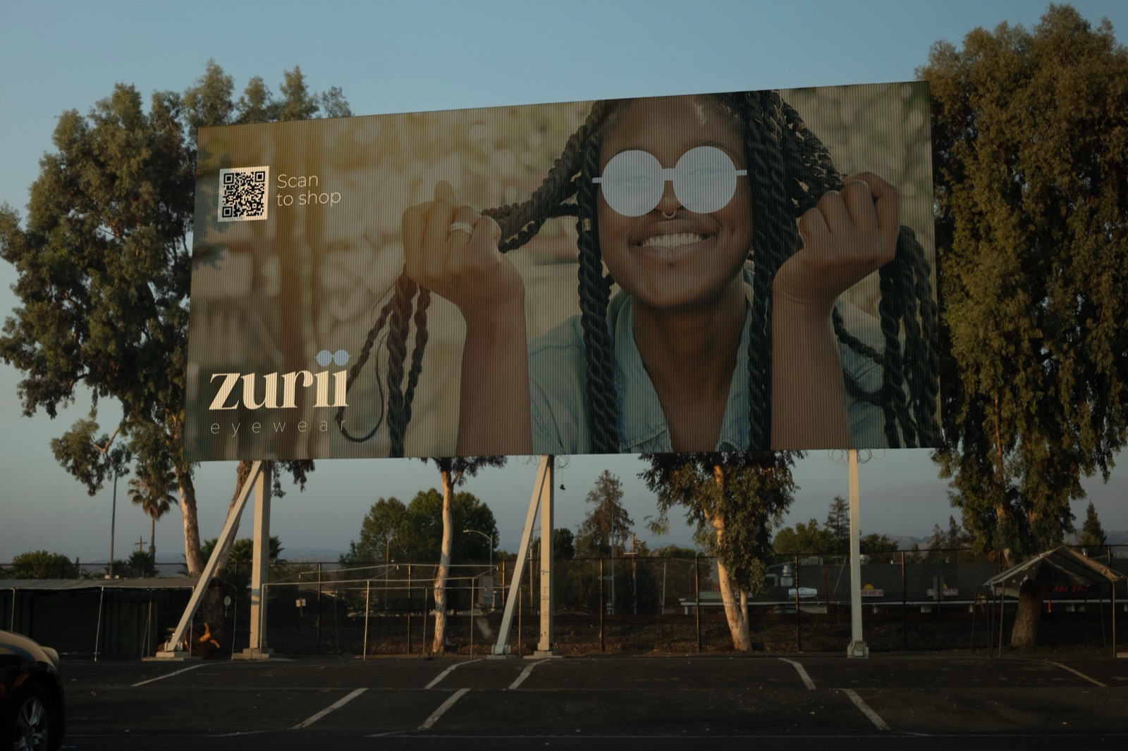Zurii Eyewear billboard with a scan to shop QR code beside a model in round sunglasses